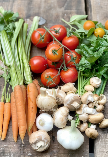 Abondance de légumes frais sur une surface en bois, incluant des tomates sur vigne, des carottes, des céleris, des champignons, et des oignons, tous éclatants de fraîcheur et prêts à être utilisés dans des plats savoureux.