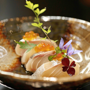"Assortiment de sashimis garnis de fleurs comestibles et d'œufs de poisson, disposés de manière artistique sur une assiette en verre noire, mettant en avant la délicatesse et la précision de la cuisine japonaise."