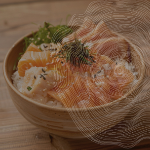 Un bol en céramique contient du riz, des tranches de poisson cru (probablement du saumon), et des légumes verts. Le bol est posé sur une table en bois. Des graines de sésame noires sont saupoudrées sur le poisson. Un motif abstrait évoquant des cernes d'arbre et des feuilles est superposé à l'image.