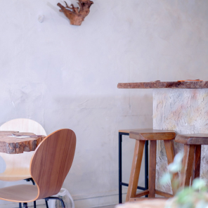 Intérieur minimaliste d'un restaurant avec une table en bois brut, chaises et tabourets en bois clair. Le décor est complété par des murs texturés et un luminaire suspendu qui offre une lumière chaleureuse.