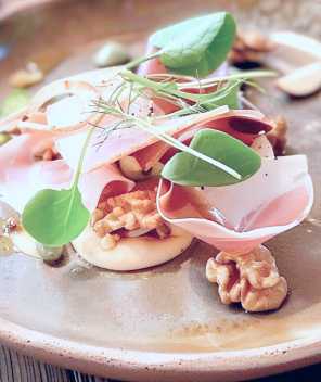 Une assiette avec une base de purée crémeuse surmontée de tranches de viande, de noix, de câpres et de verdure.