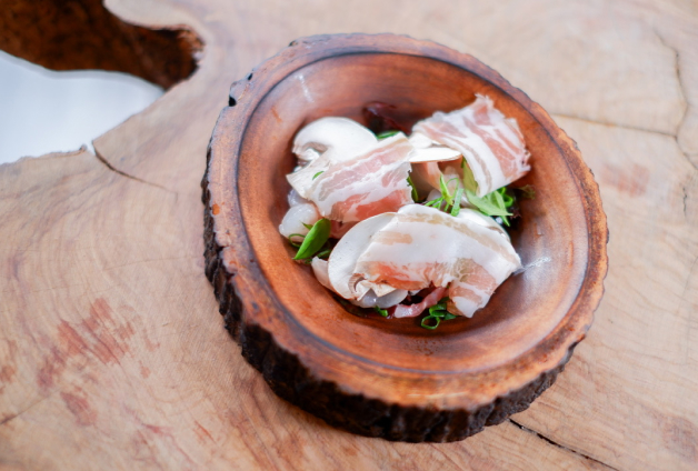 Un petit bol en bois rempli de lardons, de champignons et d'oignons verts finement tranchés, reposant sur une table en bois rustique.