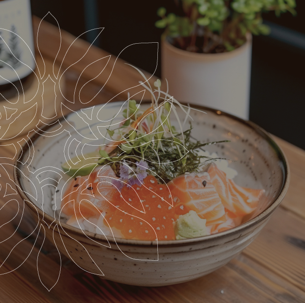 Un bol en céramique contient du riz, des tranches de saumon cru, des œufs de saumon, des tranches d'avocat et des micro-pousses. Le bol repose sur une table en bois. Des graines de sésame sont saupoudrées sur le saumon. Un motif de feuille de monstera stylisée est superposé à l'image.